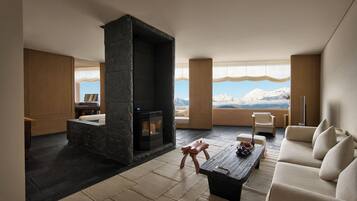 Una sala de estar moderna con chimenea de piedra, un sofá, una mesa de centro y vistas a montañas a través de amplios ventanales.