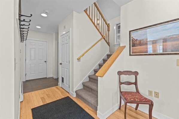 A staircase with wooden handrails, a wooden chair, and a framed picture on the wall. - Little River Retreat - Comfort & Style in Stowe (Stowe)