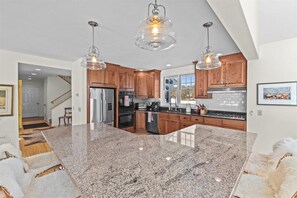 A modern kitchen with granite countertops, wooden cabinets, and pendant lighting. - Little River Retreat - Comfort & Style in Stowe (Stowe)
