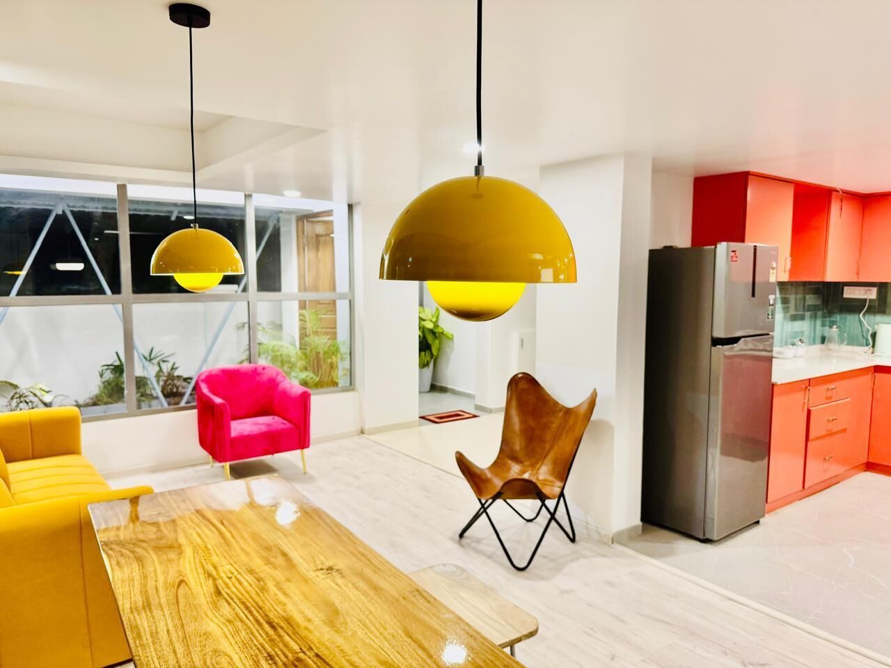 Une cuisine moderne équipée d’un réfrigérateur, de meubles de rangement orange et d’un coin repas avec une table en bois et deux chaises.