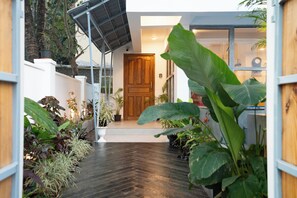 A narrow, wooden-floored hallway with a wooden door at the end, surrounded by various potted plants. - Mela By Half (Calangute)