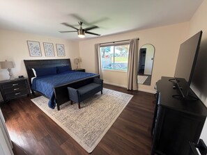 A bedroom with a bed, bedside tables, a ceiling fan, a large window with curtains, a mirror, and a TV. - Charming golf course home in Tempe, everything you need for a relaxing stay (Tempe)