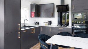 A modern kitchen with dark cabinetry, a white countertop, a black microwave, and a dining area with a white table and black chairs. - 2 bedroom accommodation in Old Langho, Ribble Valley (Old Langho, Ribble Valley)