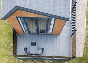 Een dakterras met een tafel en stoelen, een houten terras en een glazen deur die naar de binnenruimte leidt.