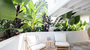 A modern outdoor seating area with two wooden chairs and a small table, surrounded by lush tropical plants. - Palm Springs by the Beach, Glam, Pet-Friendly, 4 Bed Retreat incl HUGE studio. (Mollymook Beach)