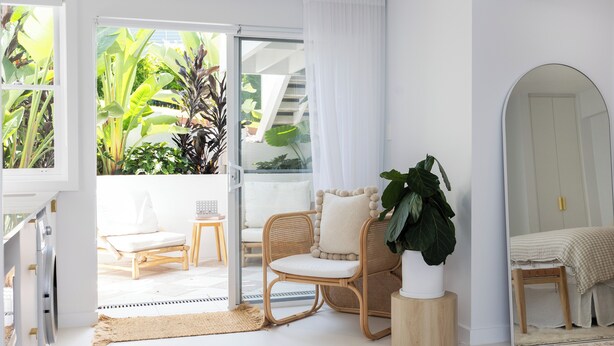 A bright, airy room with a sliding glass door leading to a balcony, wicker furniture, and a large potted plant. - Palm Springs by the Beach, Glam, Pet-Friendly, 4 Bed Retreat incl HUGE studio. (Mollymook Beach)