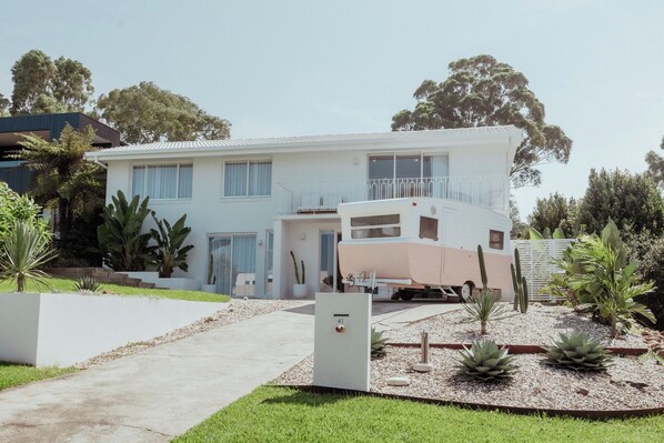 Une maison à deux étages avec une allée, un camping-car garé et diverses plantes.