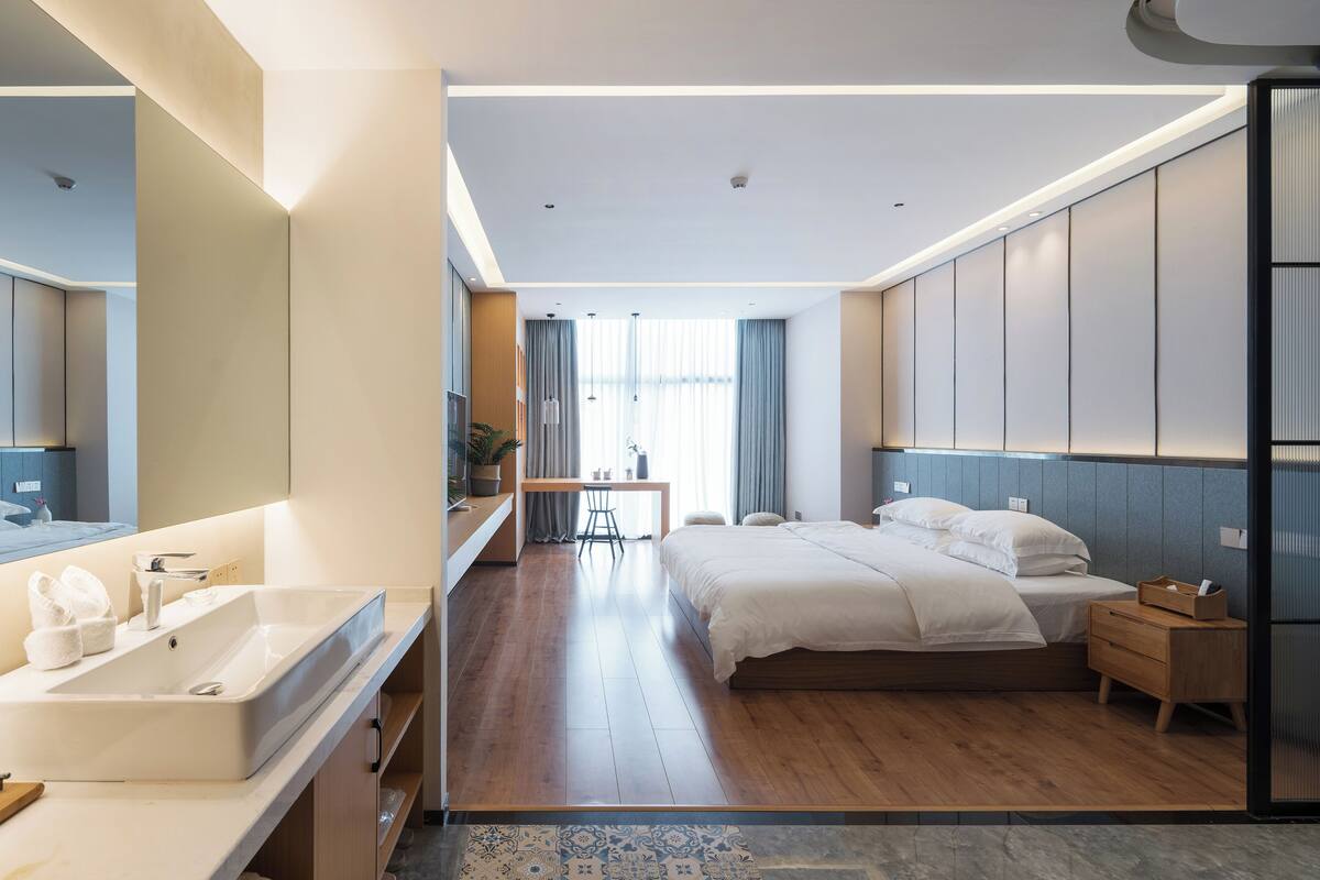 Une chambre d’hôtel moderne dotée d’un grand lit, d’une table de chevet, d’un bureau et d’une salle de bain avec un lavabo et un miroir.
