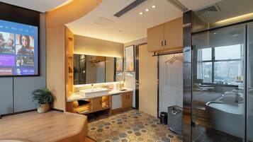 A modern bathroom with a large mirror, dual sinks, a glass shower enclosure, and a view of the city through the window.