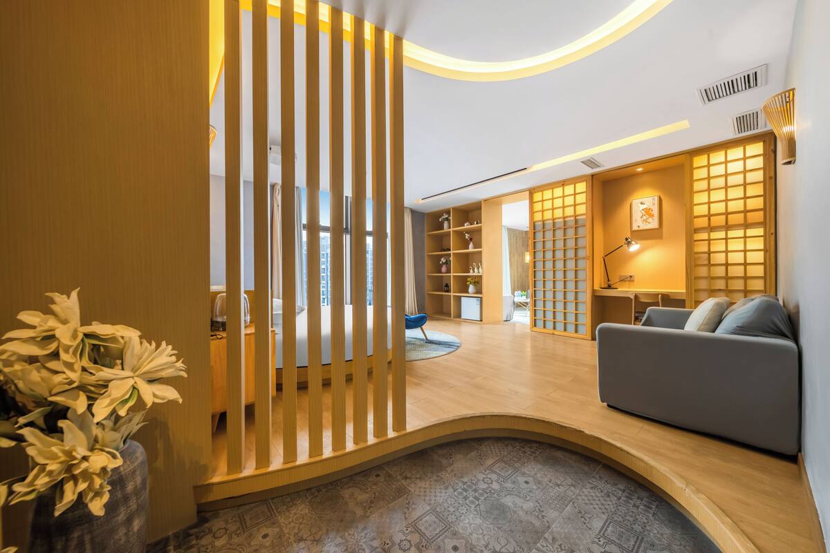 Un intérieur moderne avec une cloison en bois aux lignes courbes, un canapé gris et une bibliothèque en bois.