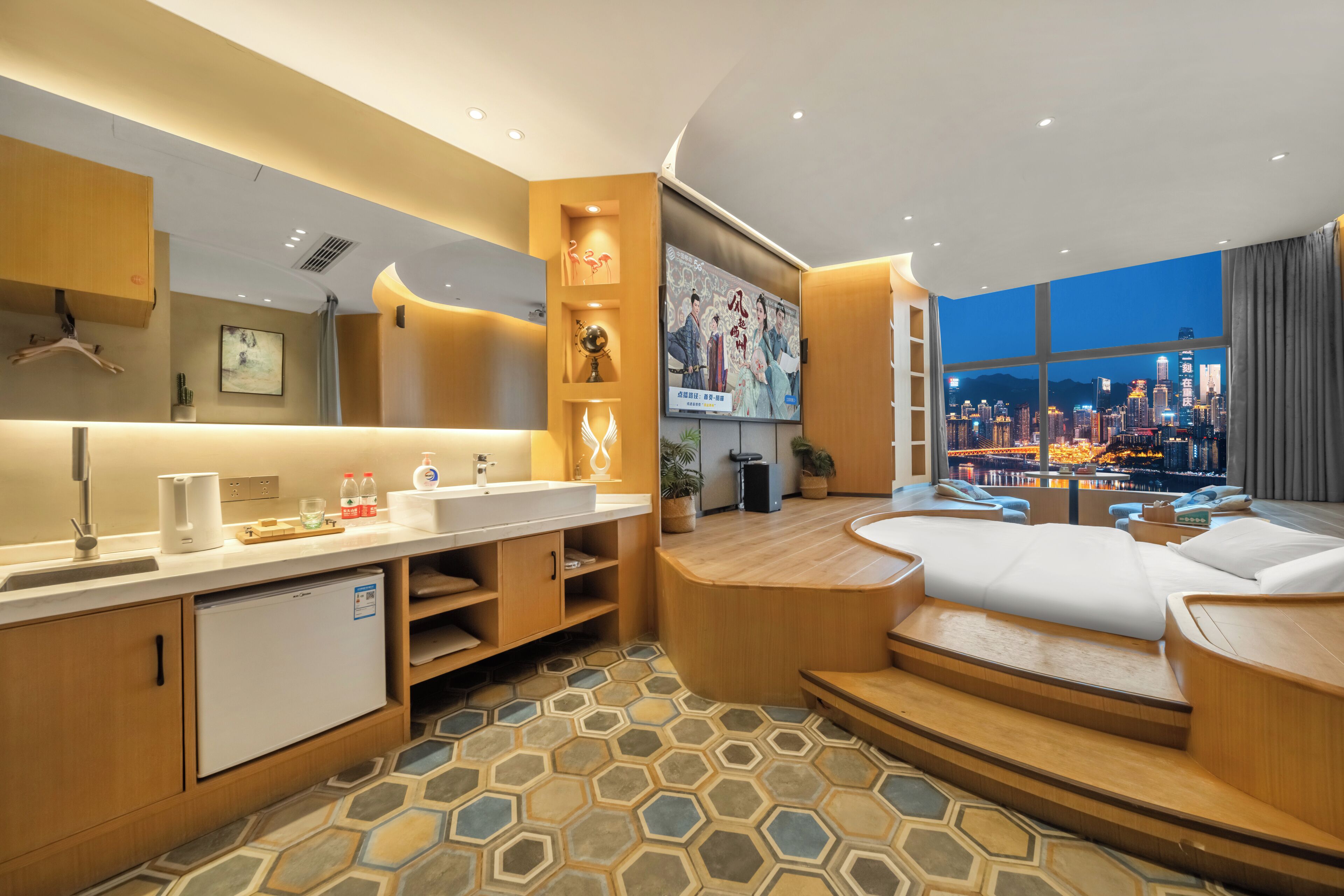 A modern hotel room with a city view, a small kitchenette, a seating area, and a large window.