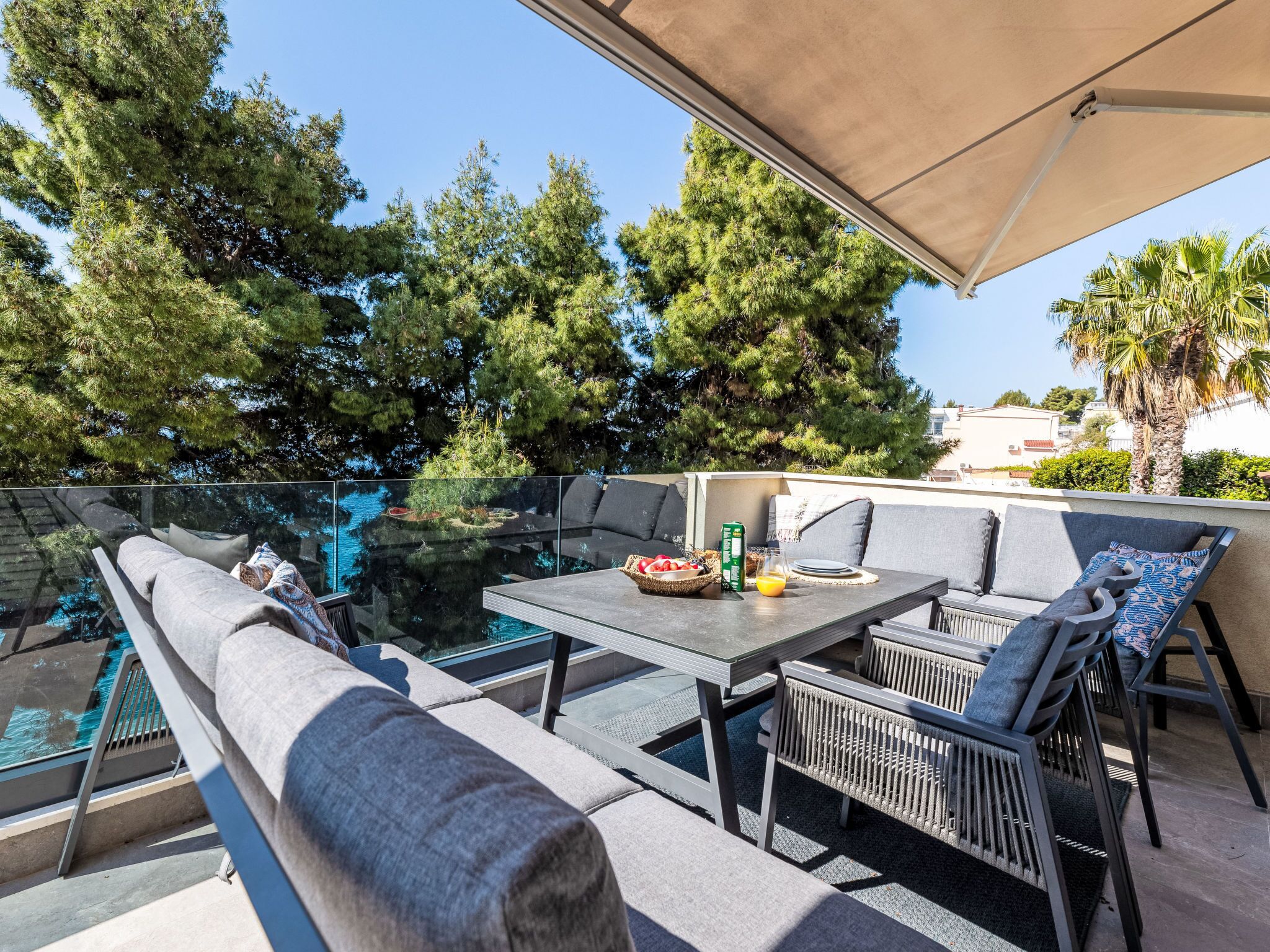 Una terraza en la azotea con barandilla de cristal, mobiliario exterior y vistas al mar y a los árboles.