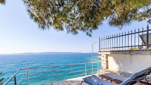A stone deck with lounge chairs overlooking a turquoise sea, a stone wall, and a metal railing. - Apartment Tina by Interhome (Trogir/Okrug Gornji)