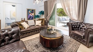 A spacious living room with a brown leather sofa, a round coffee table, and a large window with sheer curtains. - Apartment Tina by Interhome (Trogir/Okrug Gornji)