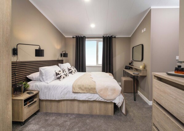 A modern bedroom with a bed, bedside tables, a desk, a mirror, and a window.