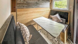 A compact, modern RV interior with a wooden accent wall, a built-in bench, a small table, and a window offering a view of greenery. - 2 bedroom accommodation in Gartmore (Gartmore)