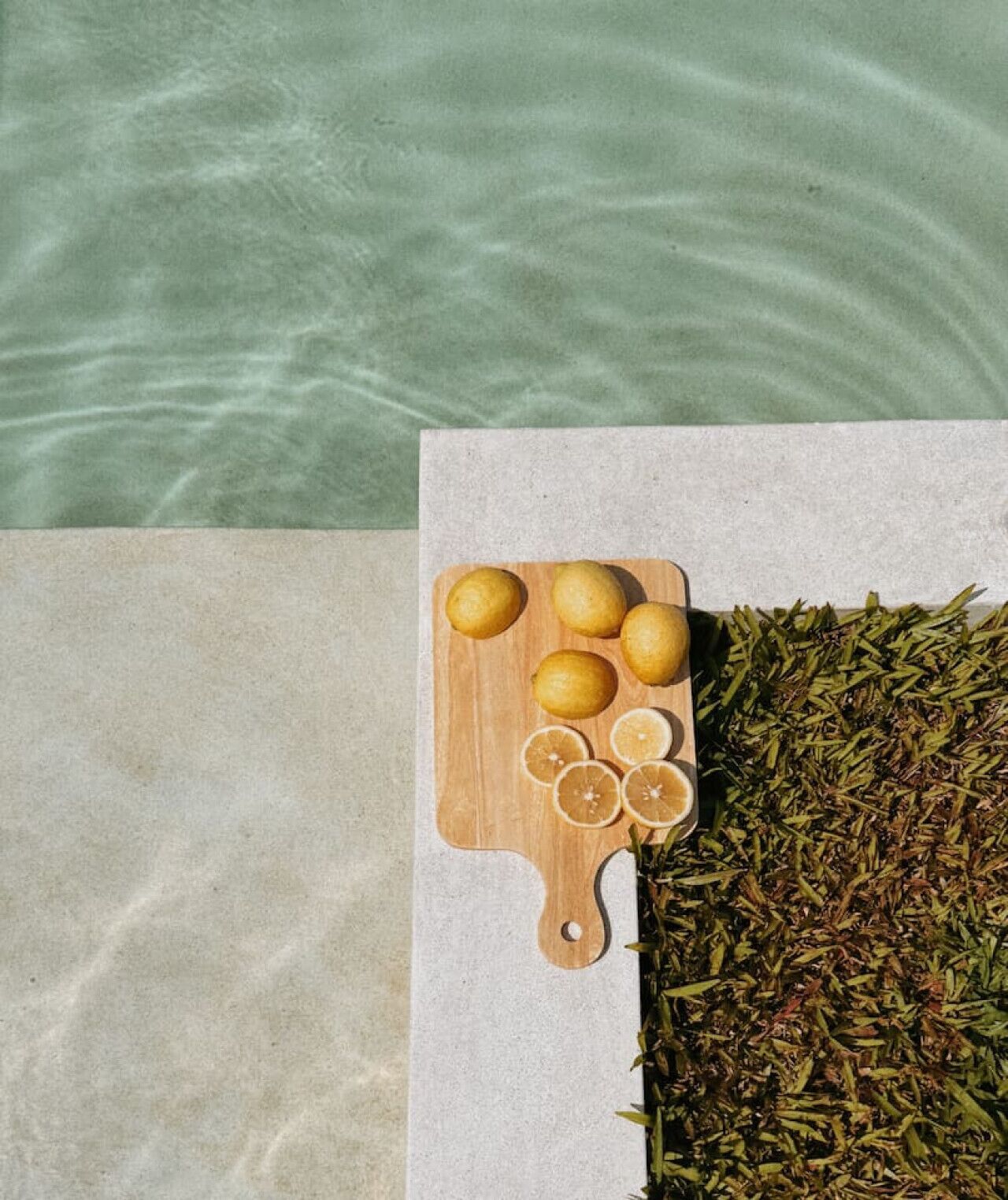 A wooden cutting board with lemons and lemon slices on a stone surface next to a pile of dried herbs.