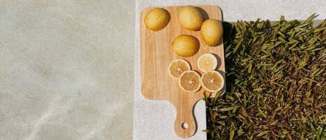 A wooden cutting board with lemons and lemon slices on a stone surface next to a pile of dried herbs.