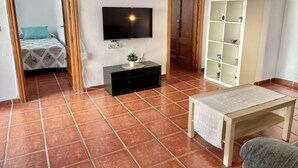 Een woonkamer met een televisie, een kleintje tafeltje, een kast en een bed op de achtergrond.