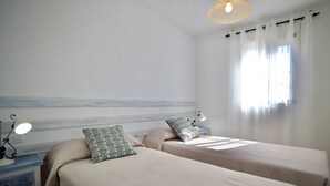 A bedroom with two beds, a nightstand with a lamp, a headboard, and a window with curtains. - R009. CASA LIDIA - House with swimming pool (Nerja)
