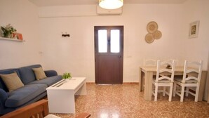 A living room with a blue sofa, a white coffee table, a wooden chair, a dining table with white chairs, a brown door, and a wall-mounted air conditioner. - R009. CASA LIDIA - House with swimming pool (Nerja)