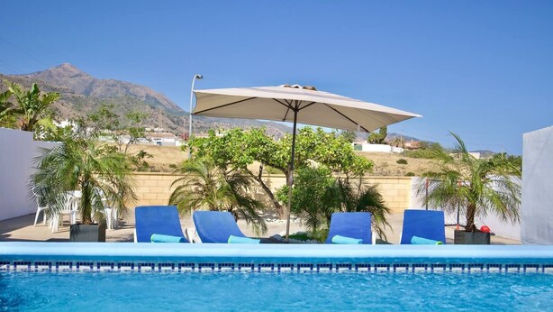 A pool area with lounge chairs and umbrellas, surrounded by palm trees and a mountain view. - R009. CASA LIDIA - House with swimming pool (Nerja)