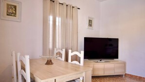 A dining area with a wooden table and chairs, a television on a cabinet, and a window with curtains. - R009. CASA LIDIA - House with swimming pool (Nerja)