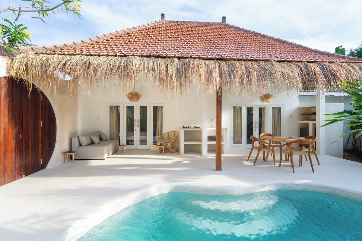 Una casa con piscina, techo de paja y valla de madera.