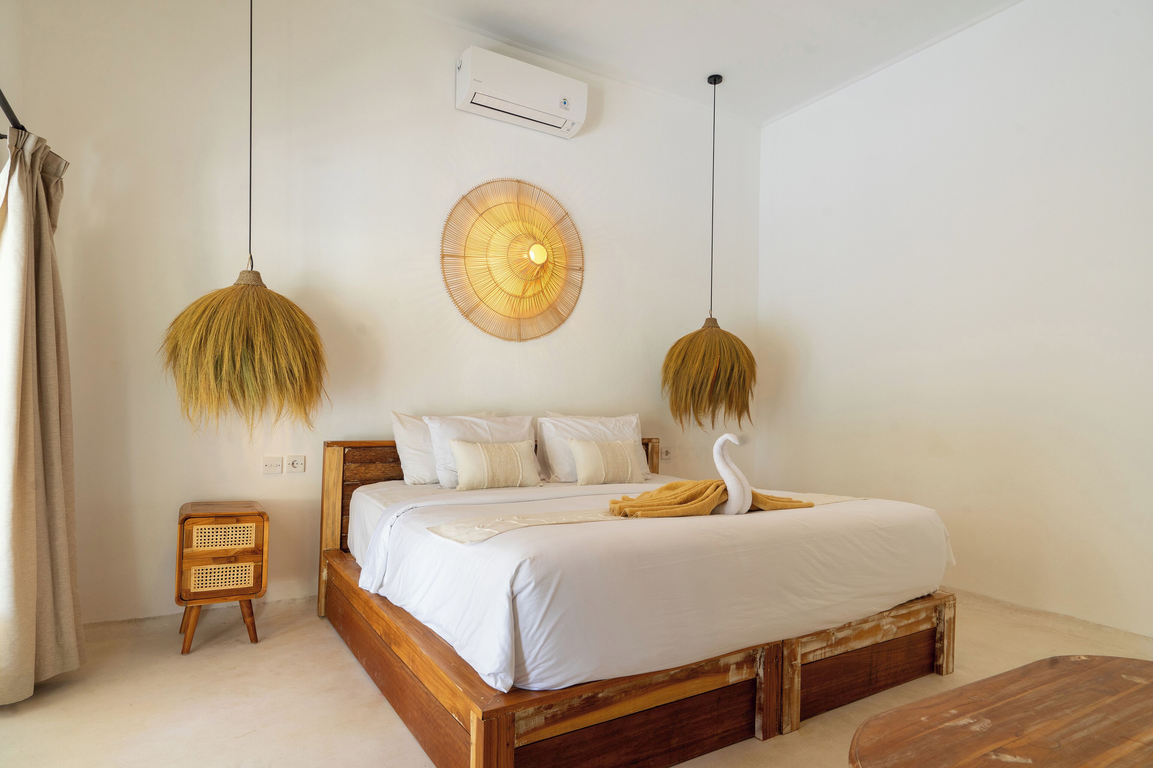 A bedroom with a wooden bed, white bedding, a wall-mounted fan, and a small wooden nightstand.
