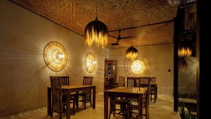 A dining area with wooden tables and chairs, a ceiling fan, and wall-mounted lamps. - Wellhouse Villas (Lembongan Island)