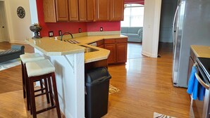 A kitchen with wooden cabinets, a granite countertop, a stainless steel refrigerator, and a built-in island with stools. - Countryside Comfort 5 MIN to FAST / WEC & 15 min HITS 1 acre 2 KNG BED Near I-75 (Ocala)