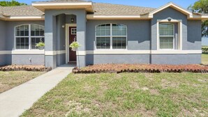 A single-story house with a gray facade, a front porch, and a small front yard with a pathway leading to the entrance. - Countryside Comfort 5 MIN to FAST / WEC & 15 min HITS 1 acre 2 KNG BED Near I-75 (Ocala)