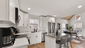 Una cocina moderna con armarios blancos, un refrigerador de acero inoxidable y una zona de bar con taburetes.