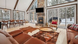 Ein geräumiges Wohnzimmer mit Kamin aus Stein, Ledersofas und großen Fenstern mit Blick auf eine verschneite Landschaft.