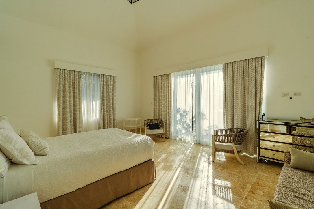 A spacious hotel room with a large bed, two chairs, a small table, and a dresser.