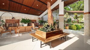 A spacious indoor area with a wooden bench, seating, and a large tree stump centerpiece. - The Village Resort Bogor Powered by Archipelago (Caringin)