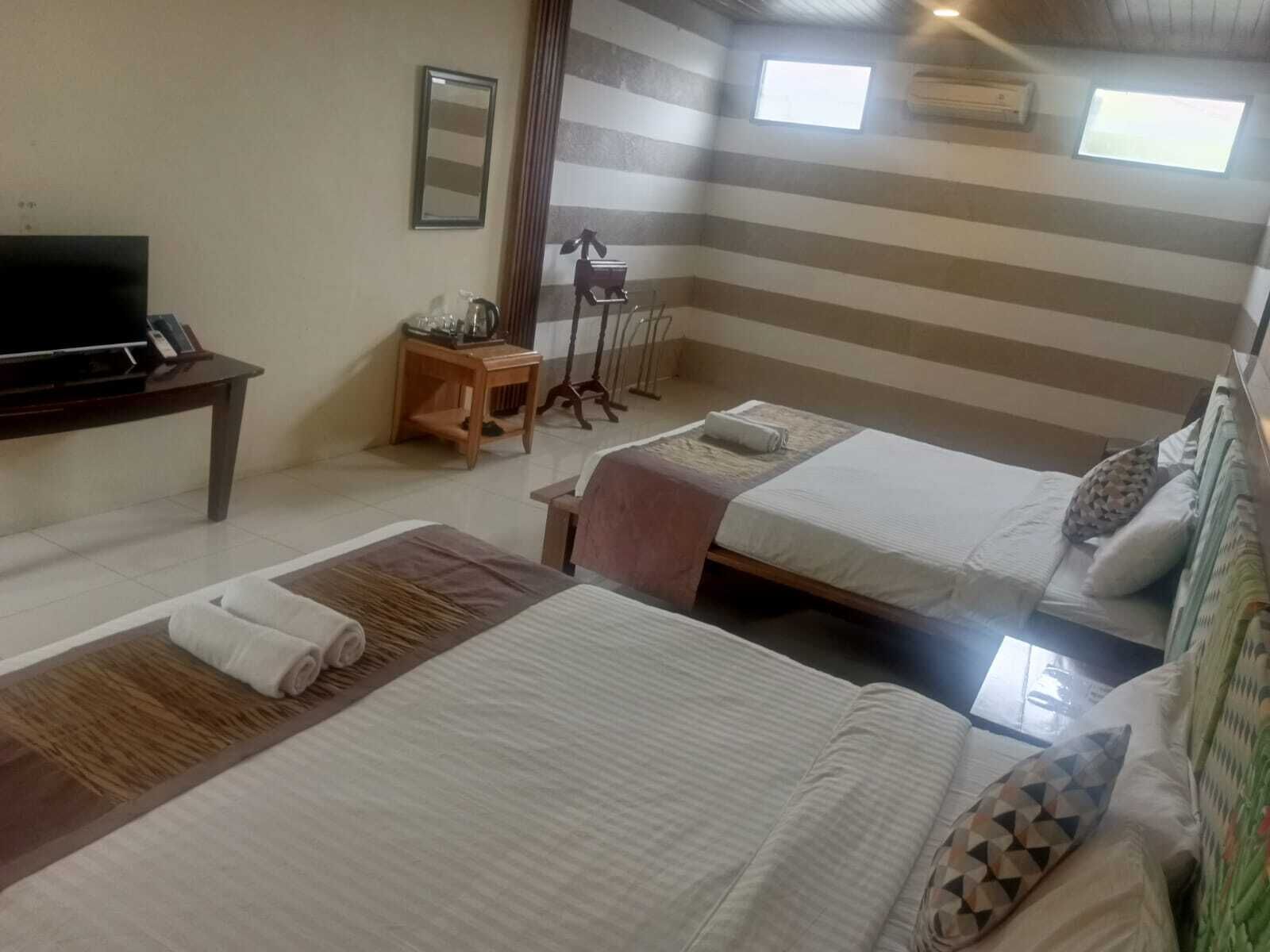 A hotel room with two beds, a TV, a small table, and a window.