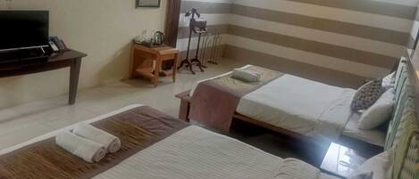 A hotel room with two beds, a TV, a small table, and a window.