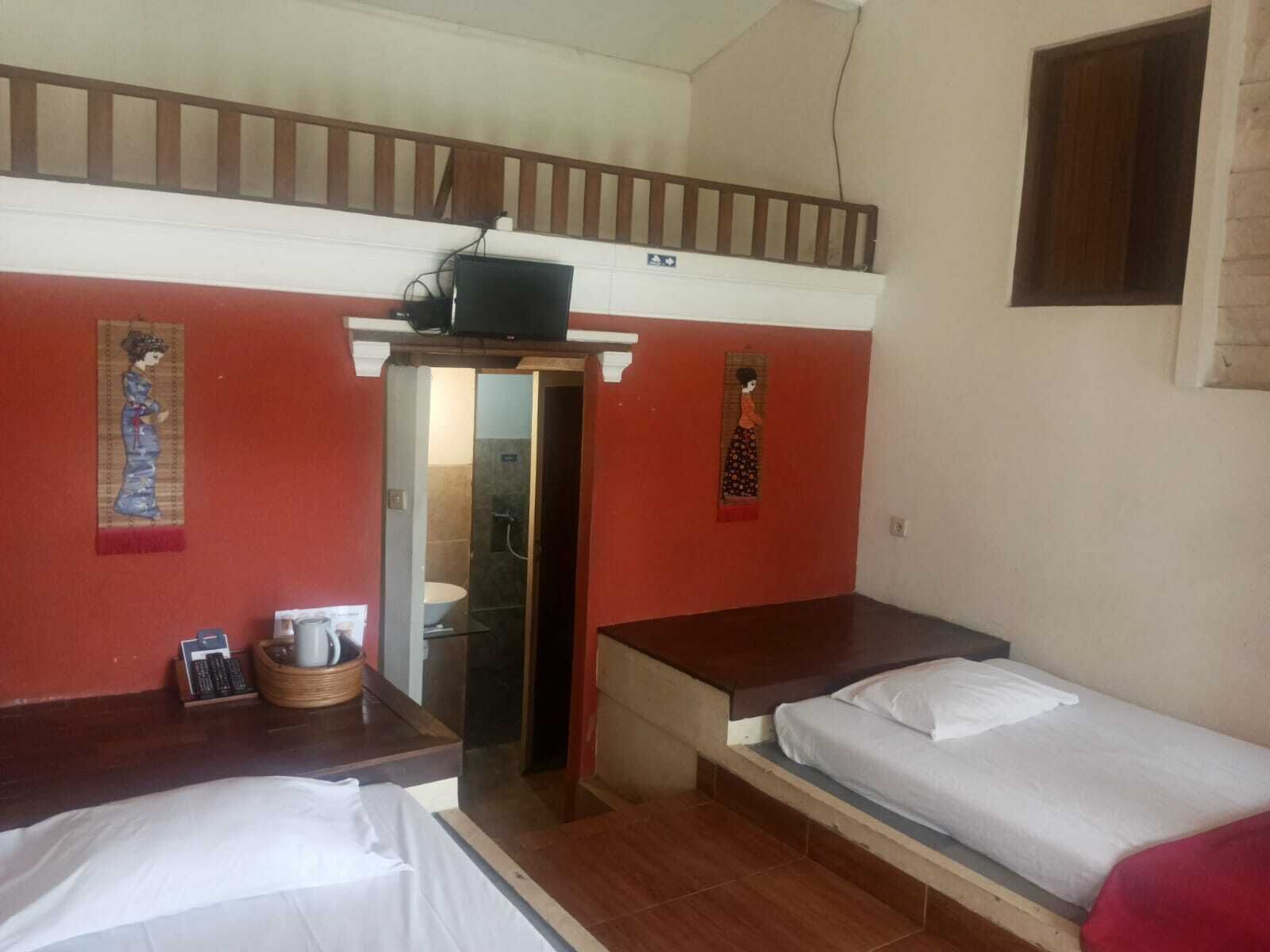 Une chambre avec deux lits, une petite table, une étagère avec une bouilloire et une porte donnant sur une salle de bain.