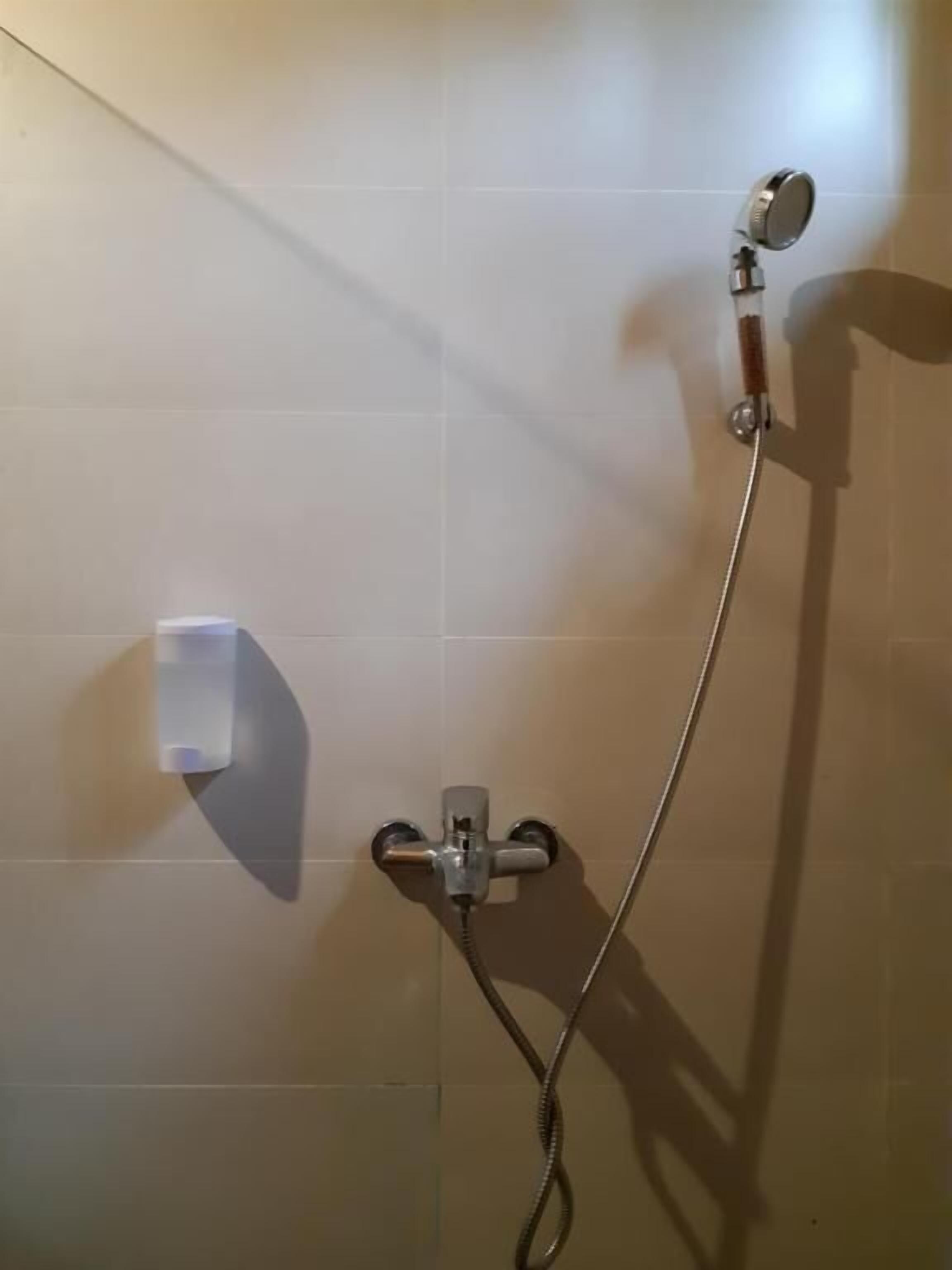 A shower with a handheld showerhead and a wall-mounted faucet.