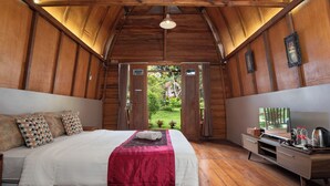 A wooden room with a bed, a desk, and a view of a garden. - The Village Resort Bogor Powered by Archipelago (Caringin)