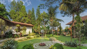 A well-maintained garden with a stone pathway, various plants, and a sign reading "The Village". - The Village Resort Bogor Powered by Archipelago (Caringin)