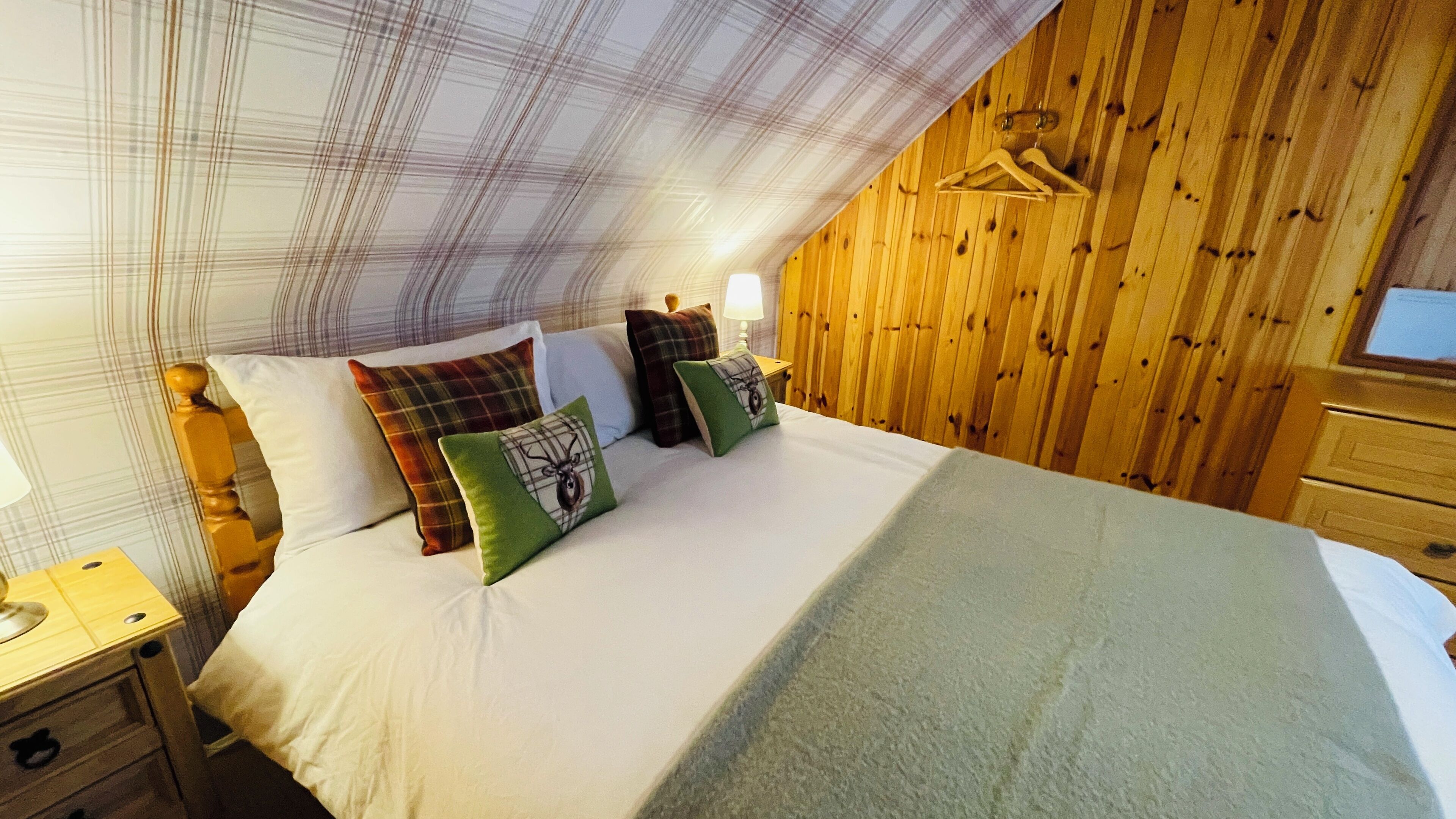 Ein Schlafzimmer mit Bett, Kissen, einem Nachttisch, einer Holzwand und einer Pendelleuchte.
