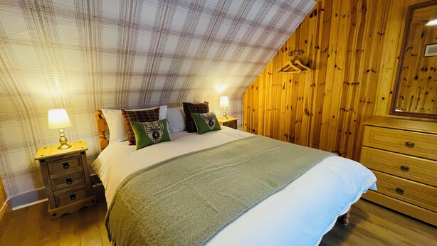 A bedroom with a bed, two bedside tables with lamps, a dresser, and a wooden wall with a hanging garment.