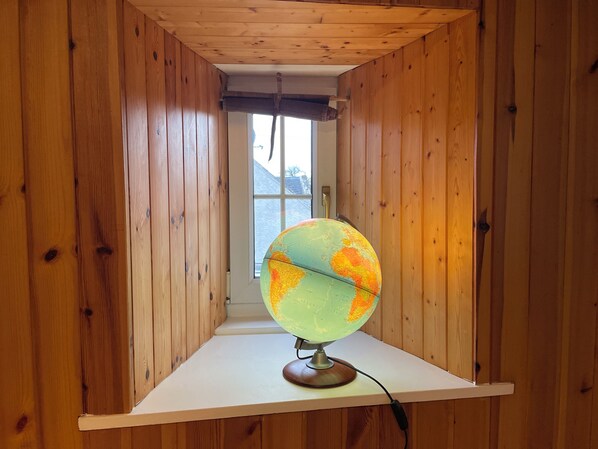 A globe on a wooden shelf in a room with wooden walls and a window.