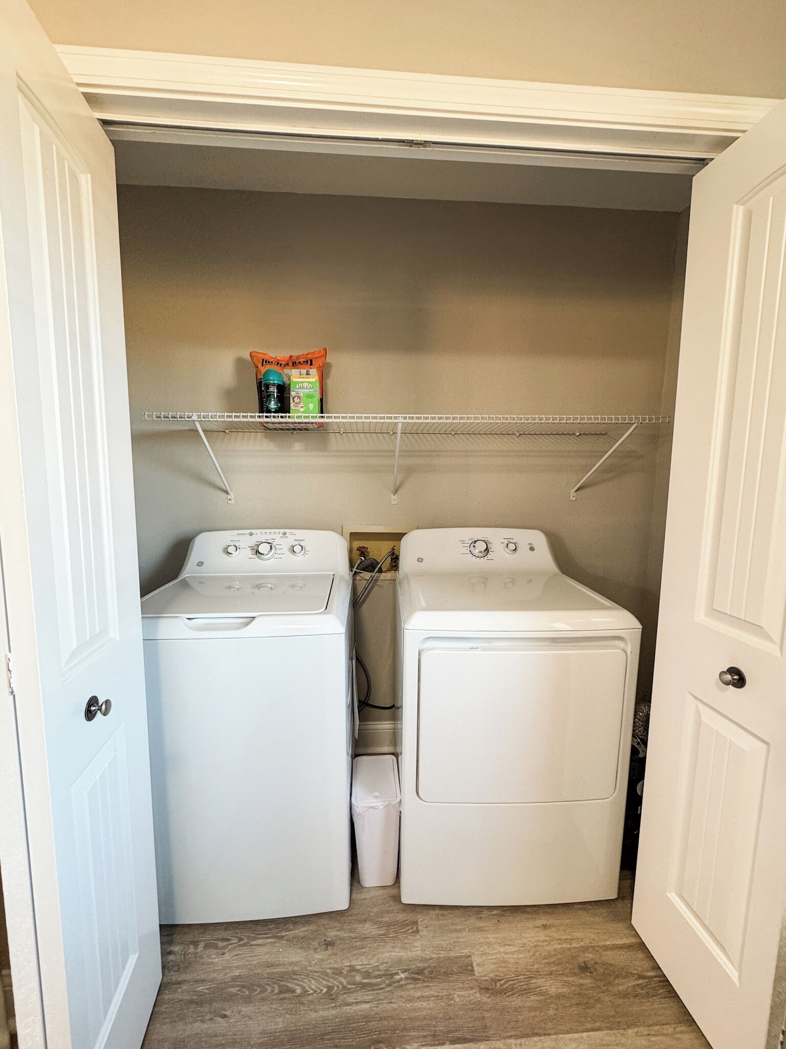 A laundry room with two white front-loading washing machines and a shelf above them holding a few items.