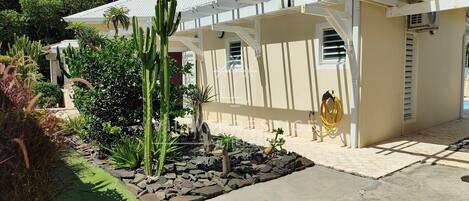 A house with a white exterior, a covered patio, and a garden with various plants and a small rock garden.