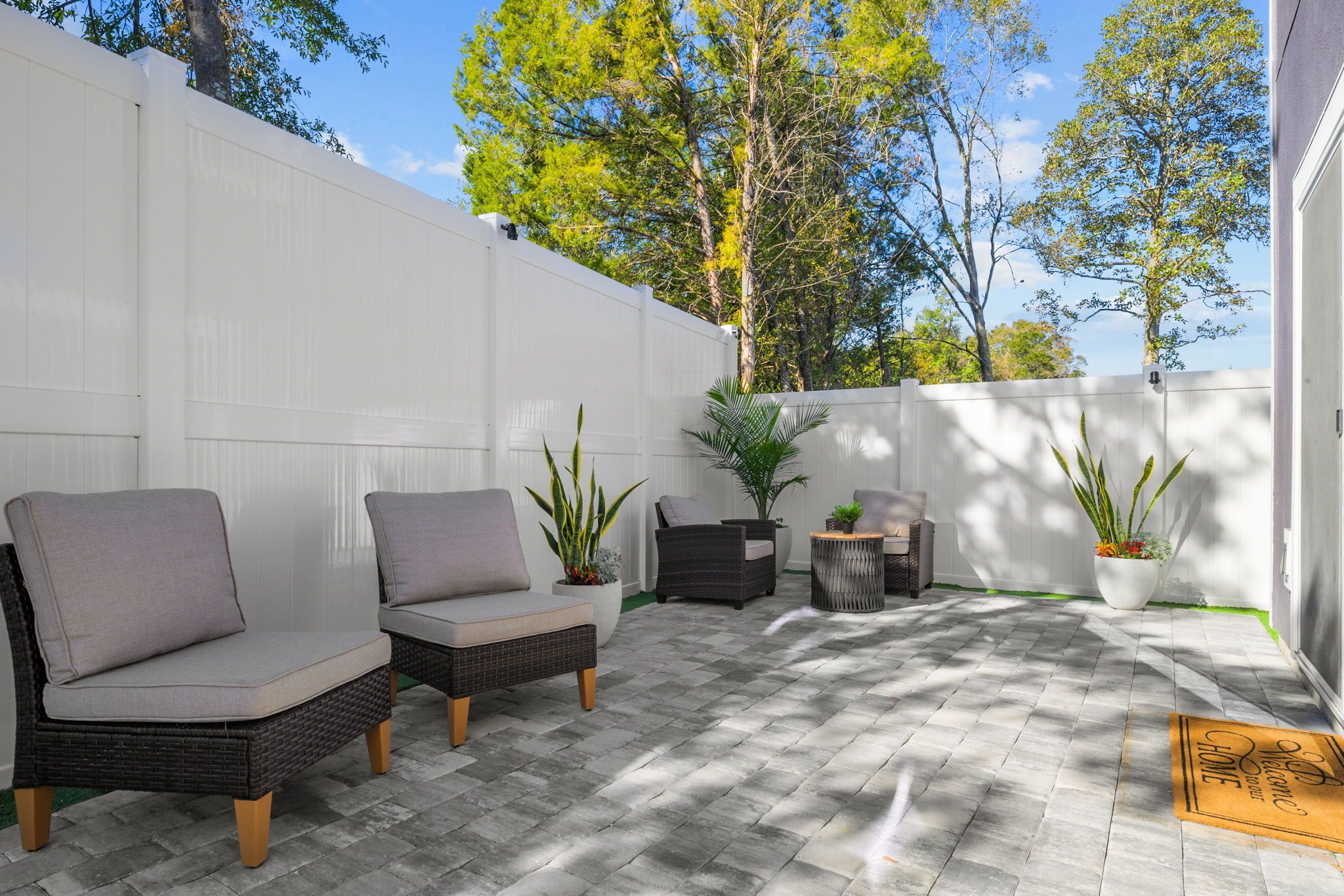 A patio area with two wicker chairs, a small round table, and potted plants.
