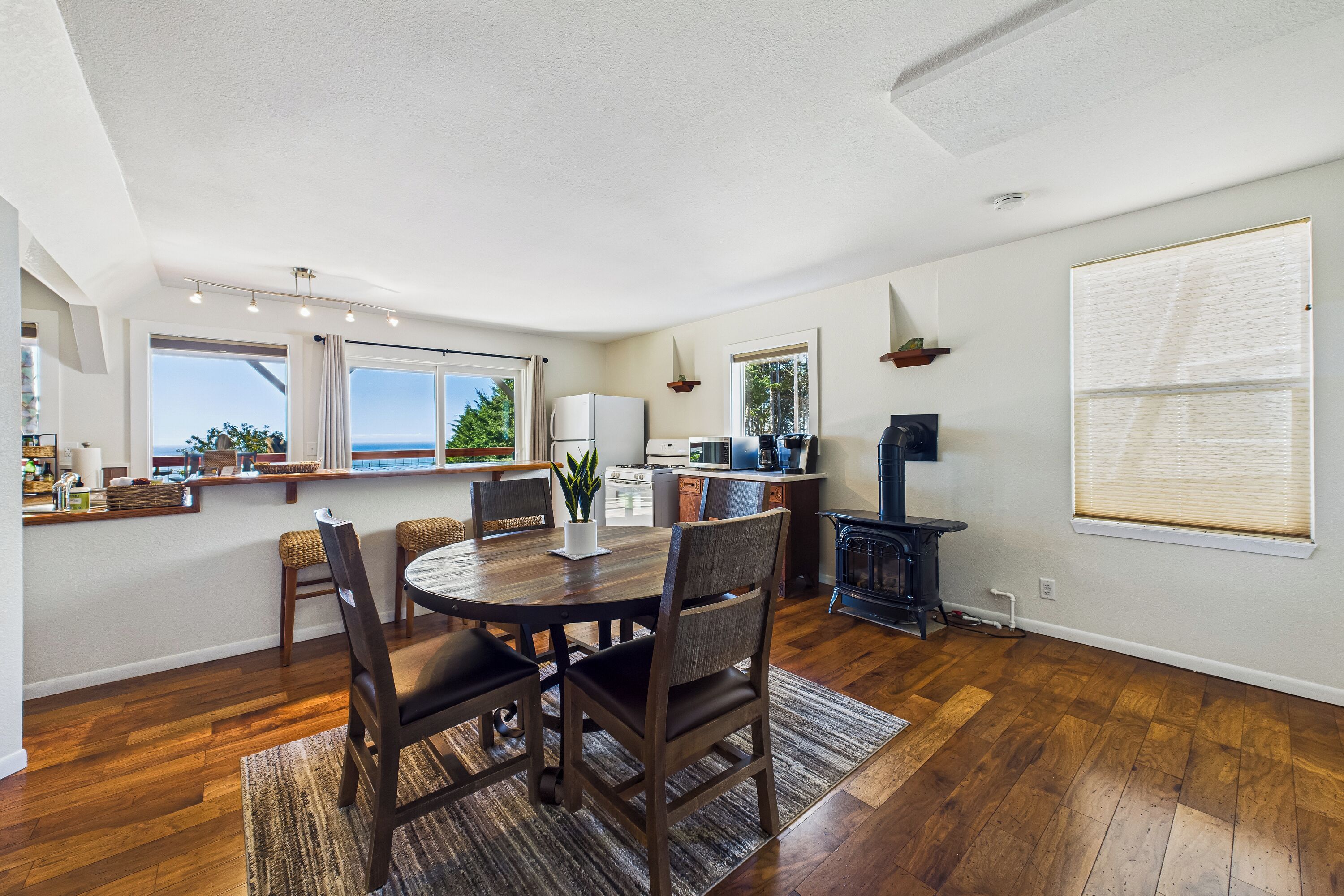 A modern kitchen with a dining area, wooden flooring, and large windows.