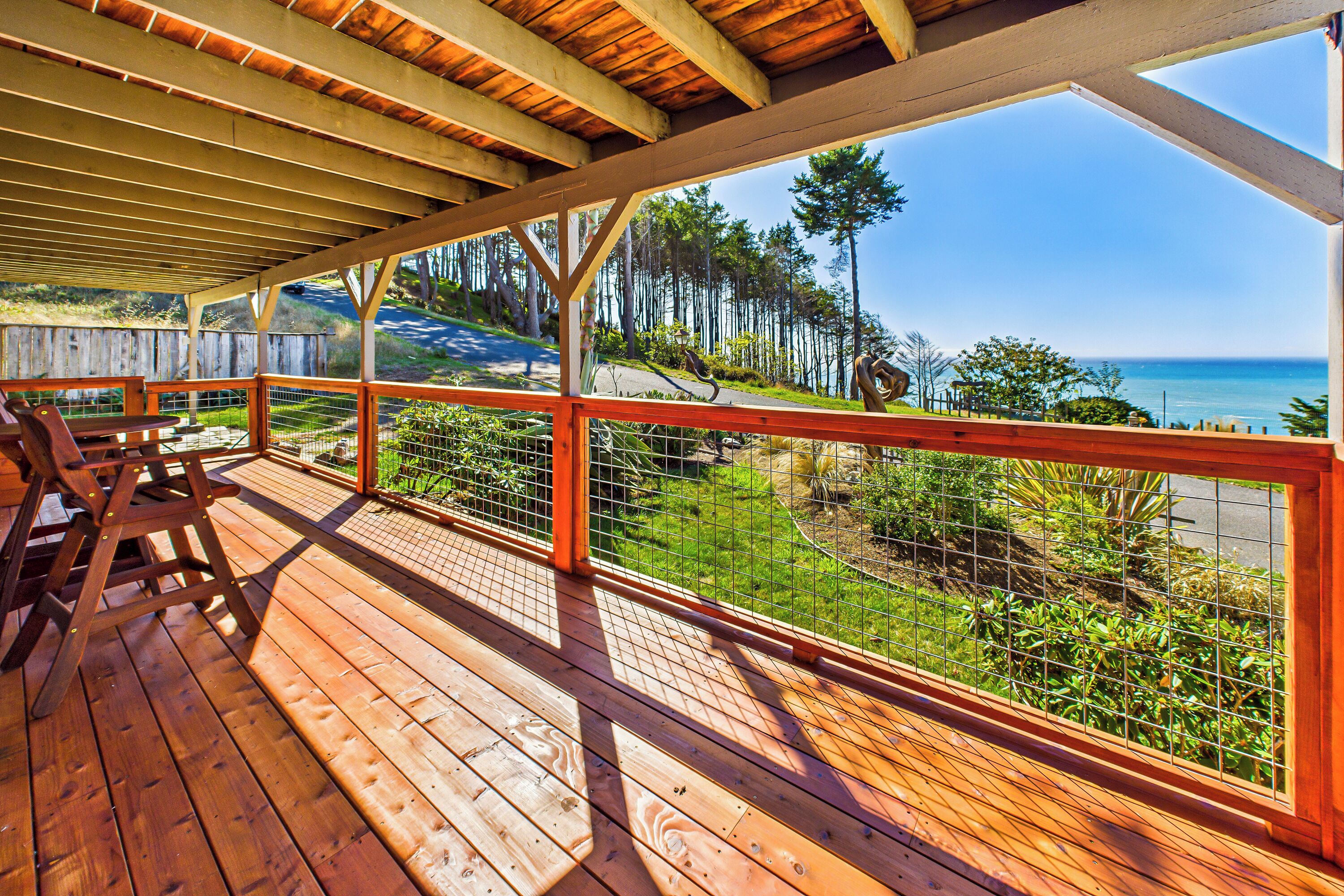 A wooden deck with a railing overlooking a coastal area with trees and a clear sky.